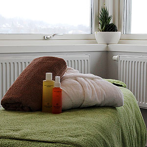 Handduk, badrock och massageolja står på massagebänk